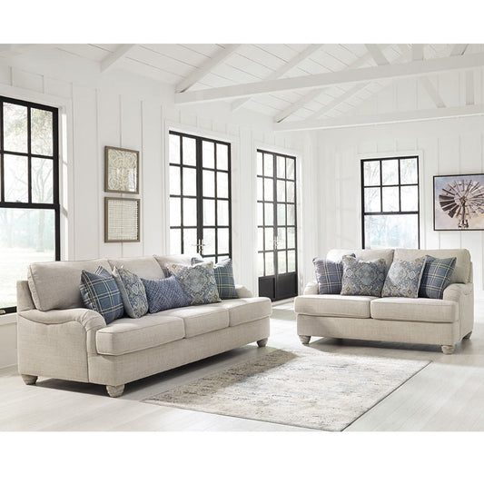 Light beige fabric sofa set with patterned throw pillows in a bright living room with white walls, black-framed windows, and a neutral rug.