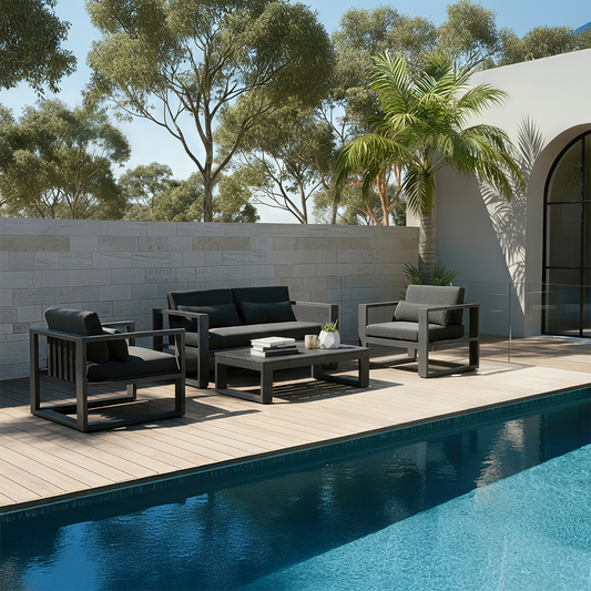 Modern black outdoor lounge set with armchairs and a coffee table beside a pool, framed by palm trees and a light stone privacy wall.