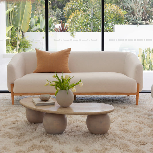 Curved white fabric sofa with timber legs in a bright, tropical-inspired living room