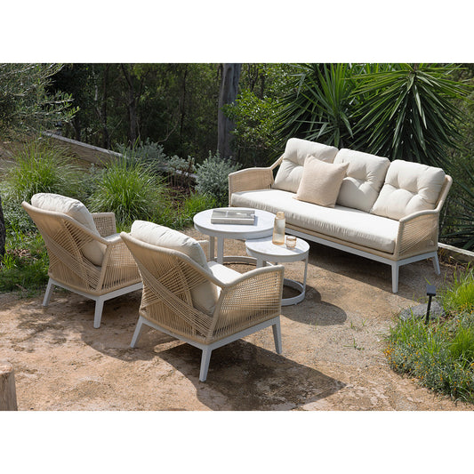 Outdoor wicker lounge set with cream cushions and round coffee table in a garden setting.