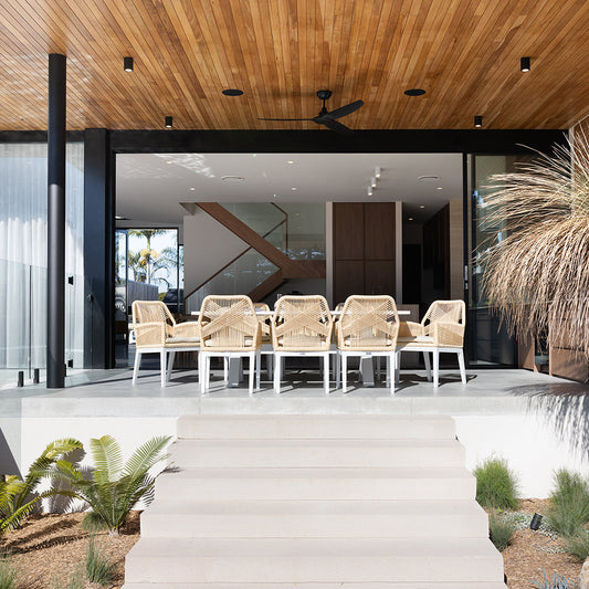 Modern outdoor dining set with woven chairs and large table under a timber ceiling patio.