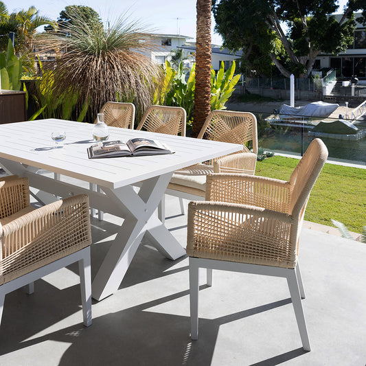 White outdoor dining table with woven dining chairs by the garden